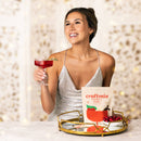 Woman in a silver dress holding a red cocktail and a 'craftmix' cranberry vanilla product.