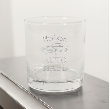 A customized tumbler glass on a silver shelf with a white background.