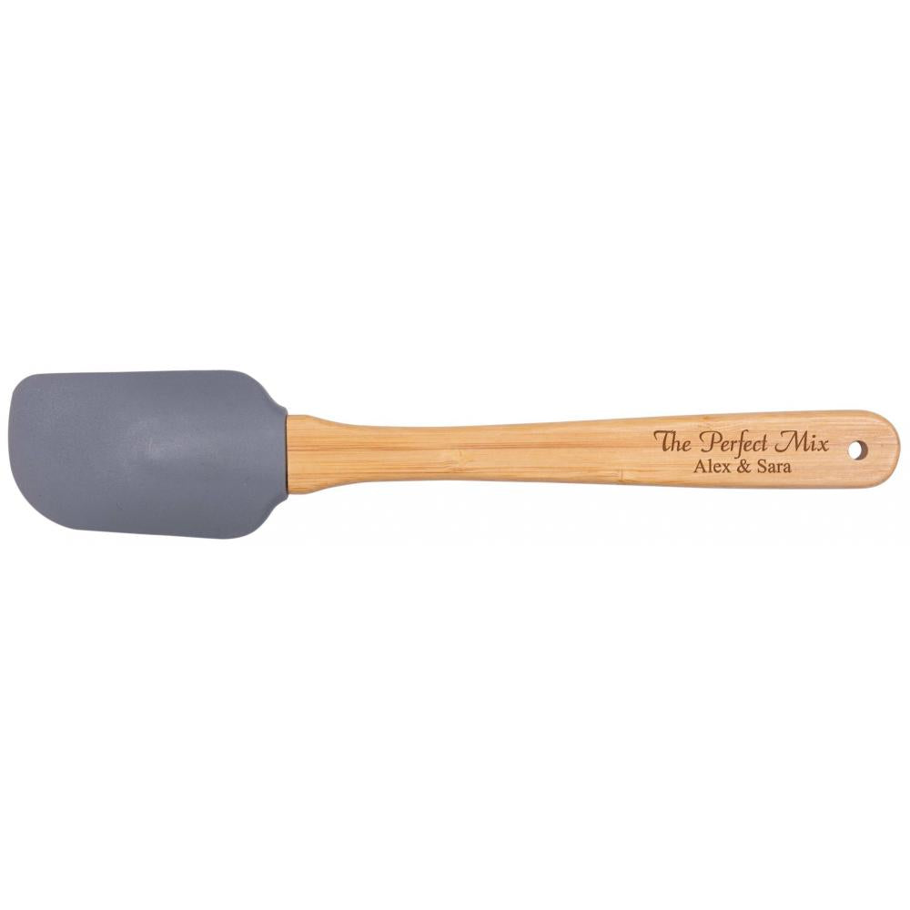 A silicon spatula with a gray head and a beige wooden handle with 'The Perfect Mix' and names 'Alex & Sara' printed on it.