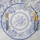 A paper placemat featuring pheasants and florals in blue and white with blue and gold flatware.
