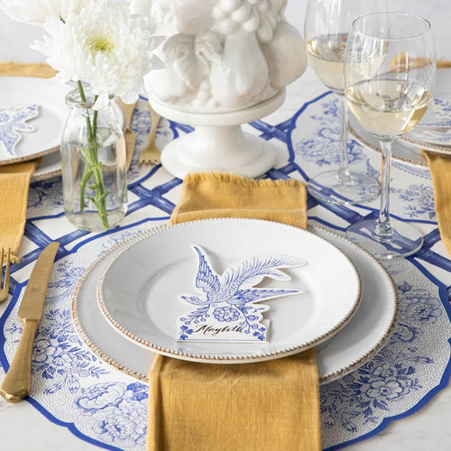 Place settings featuring paper placemats with pheasants and florals in blue and white with blue and gold flatware.