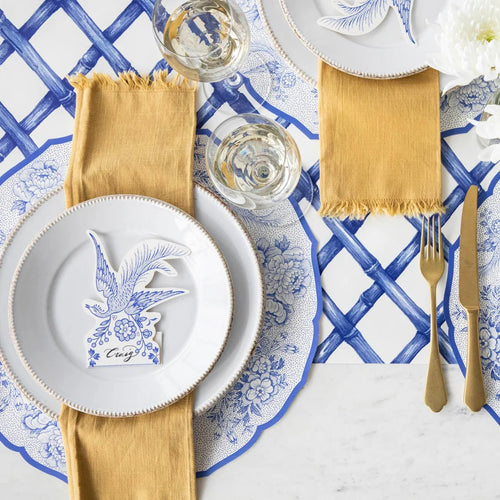 Place settings featuring paper placemats with pheasants and florals in blue and white with blue and gold flatware.