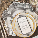 A place setting featuring gold rimmed plates, a decorative brown and beige table runner, a place card, silverware, and a black and white placemat with a regal crest style illustration featuring a lion on one side and a unicorn on the other.