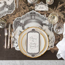 A place setting with a black and white placemat with a regal crest style illustration featuring a lion on one side and a unicorn on the other, with gold rimmed plates, a place card, silverware, and glasses.
