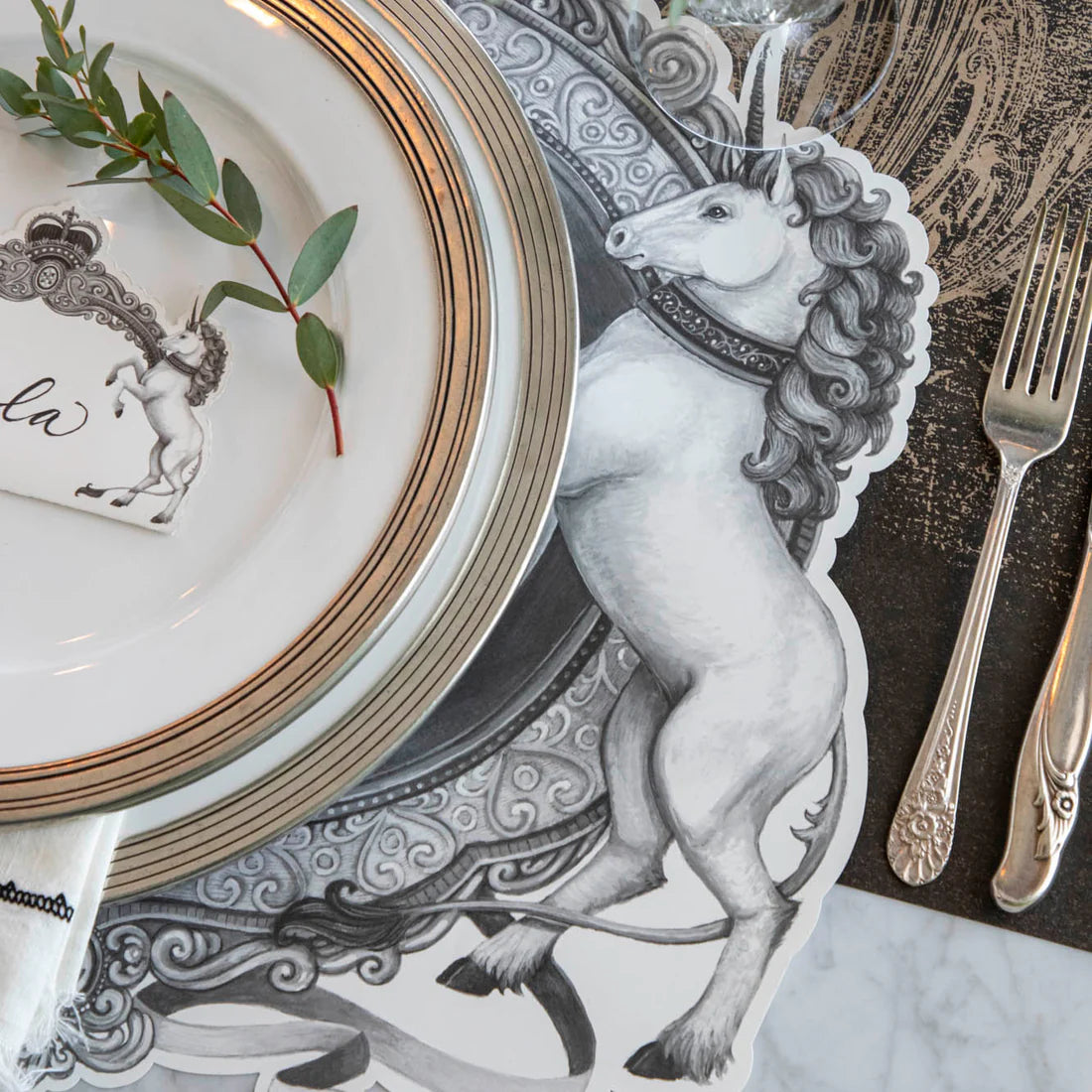 A black and white unicorn illustration as part of a placemat with gold rimmed plates on top.
