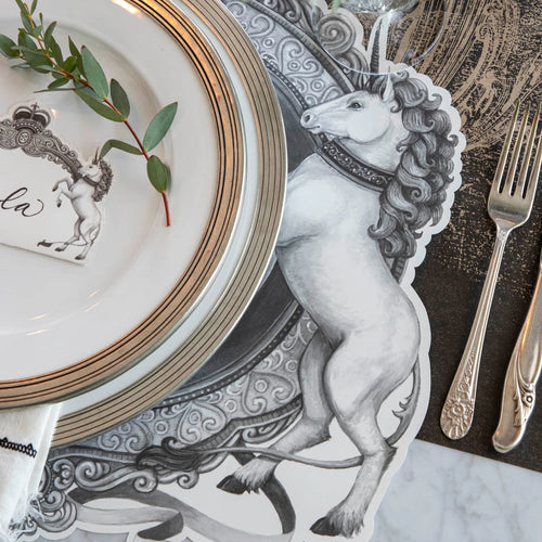 A black and white unicorn illustration as part of a placemat with gold rimmed plates on top.