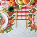 Two place settings with tomato-themed placemats and napkins with gold cutler and a bowl of tomatoes.