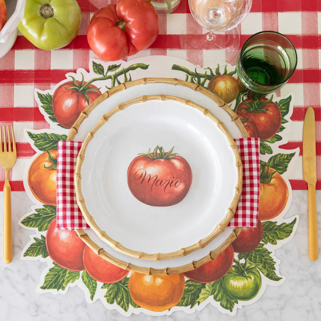 A place setting with tomato placemat, red check table runner, gold cutlery, and plates.