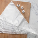 Clear plastic cake decorating bags with three white decorating nozzles  on a wooden cutting board on a marble surface.