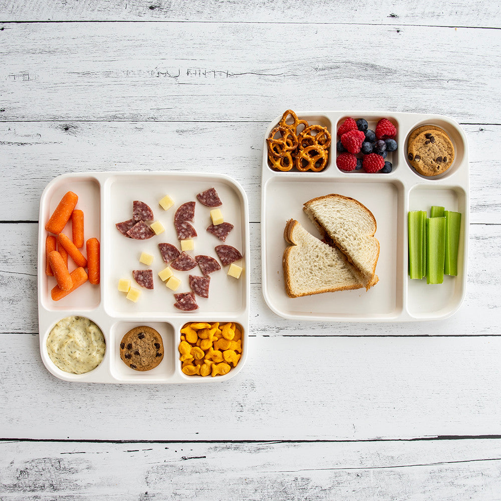 Children's lunch tray with various food items on a white wooden surface
