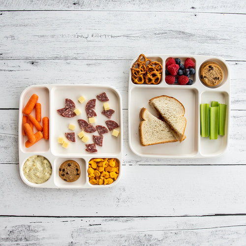 Children's lunch tray with various food items on a white wooden surface