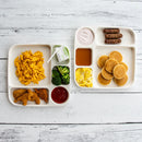 Two dinner trays with various food items on a white wooden surface
