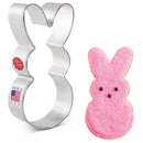 Metal bunny-shaped cookie cutter next to a pink bunny-shaped cookie on a white background