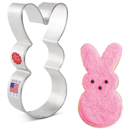 Metal bunny-shaped cookie cutter next to a pink bunny-shaped cookie on a white background