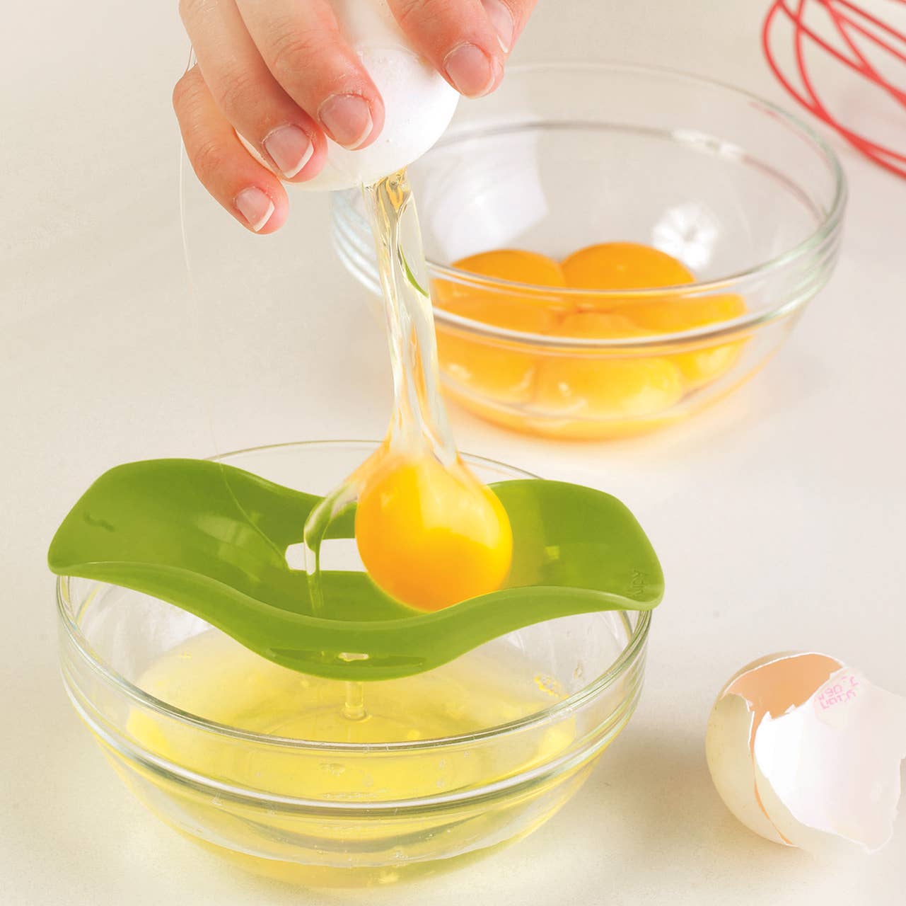 Person using a green egg separator to separate yolks into a glass bowl.