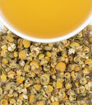 A close up look at a cup of chamomile tea and the flowers that make up the tea.