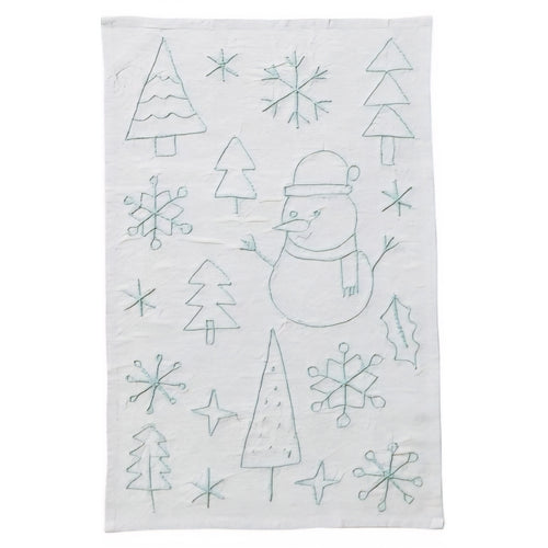 Tea towel with embroidered snowman, trees, and snowflakes on a white background