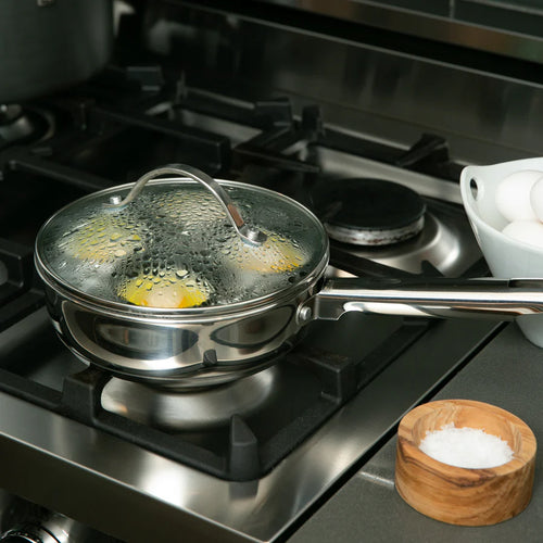 Stovetop with a egg poacher containing eggs and a wooden bowl of salt.