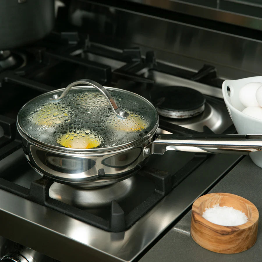 Stovetop with a egg poacher containing eggs and a wooden bowl of salt.