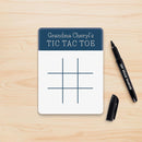 Tic Tac Toe game board with 'Grandma Cheryl's' text on a wooden surface with dry erase markers.