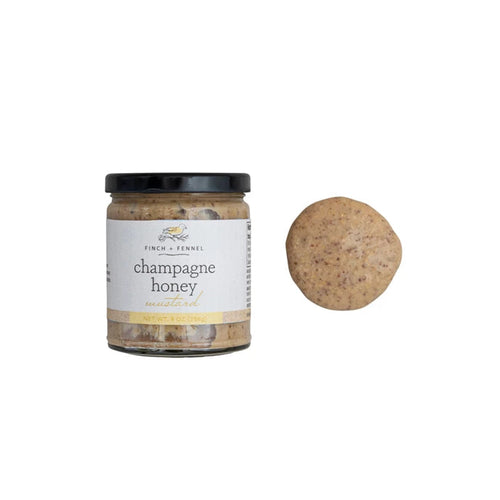 A jar of Finch & Fennel Champagne Honey Mustard with a spice grinder next to it.
