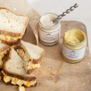 Sandwiches with mustard on a wooden board next to jars of creamy horseradish and pub mustard.