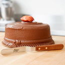 Chocolate cake with a strawberry on top and a knife next to it on a wooden surface.