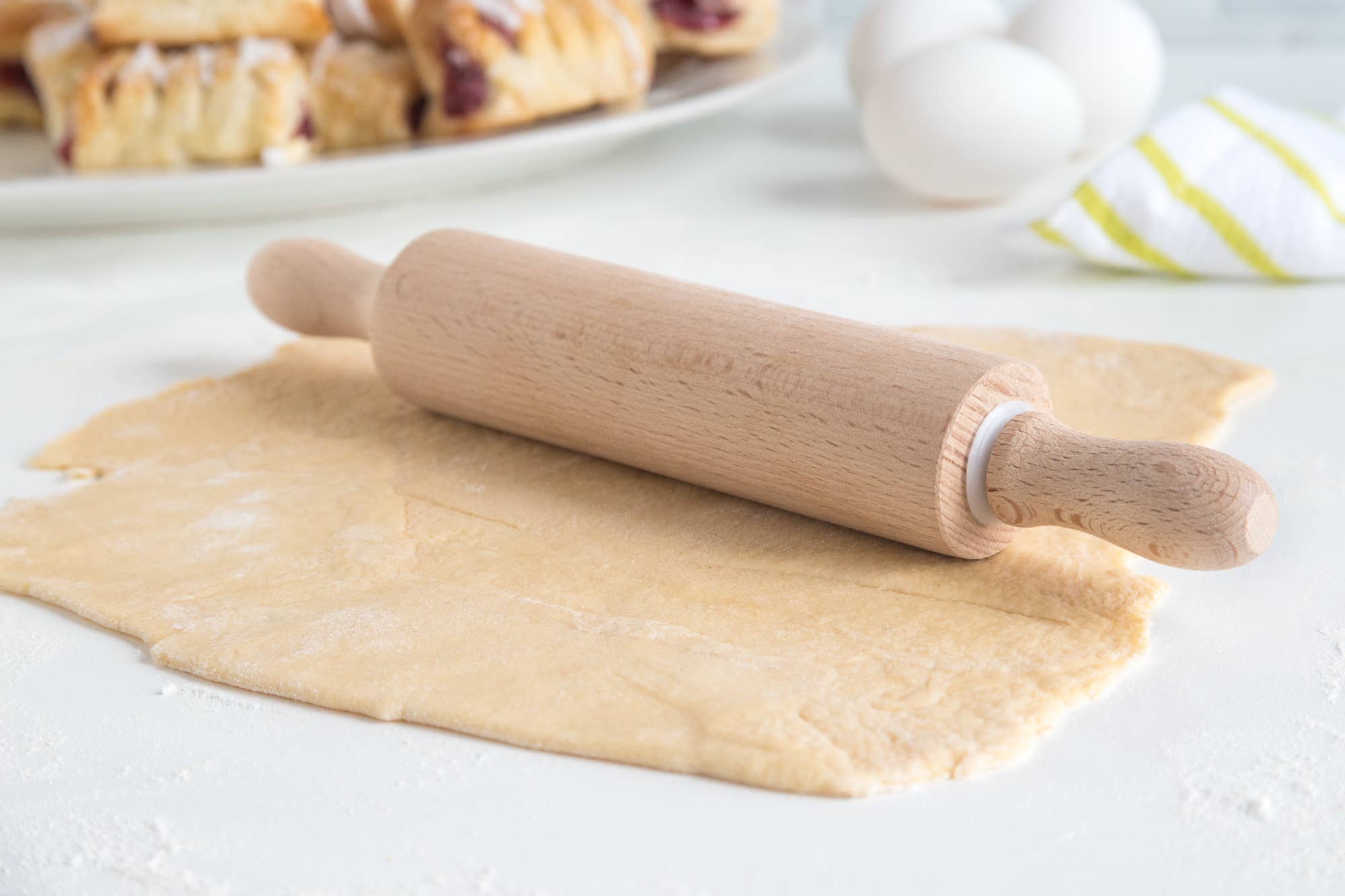 Wooden rolling pin on rolled-out dough with pastries in the background