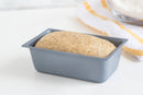 Unbaked bread dough in a loaf pan on a white surface with a yellow and white striped cloth in the background.
