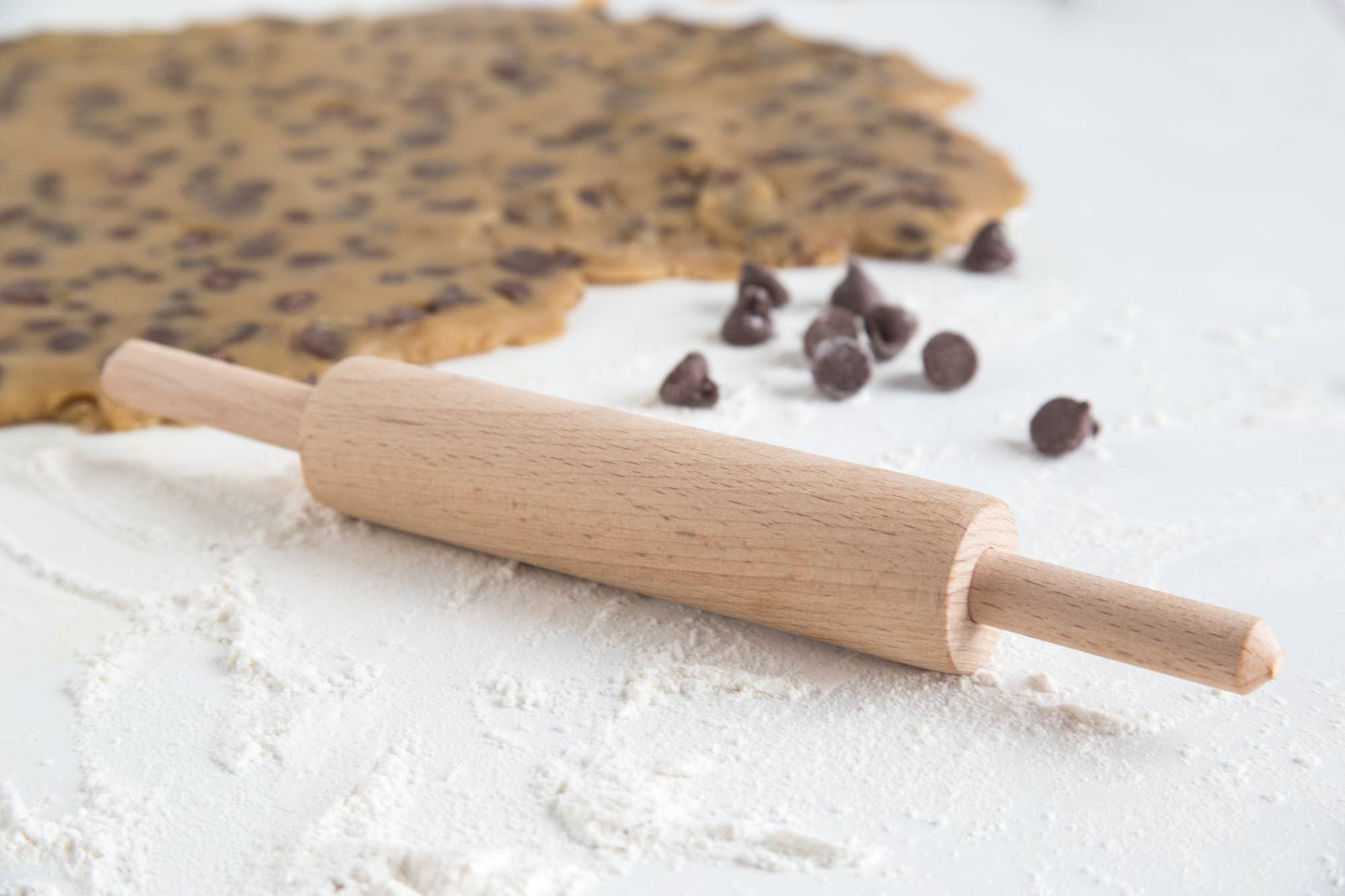 Wooden rolling pin on a surface with cookie dough and chocolate chips.
