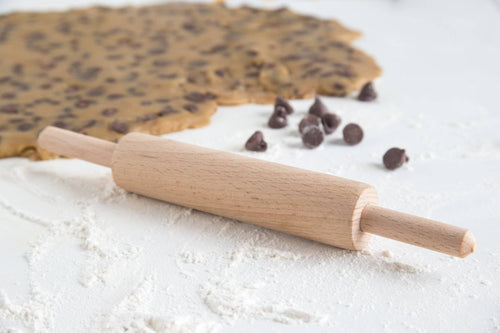 Wooden rolling pin on a surface with cookie dough and chocolate chips.