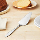 Stainless steel cake server on a wooden table with cakes in the background
