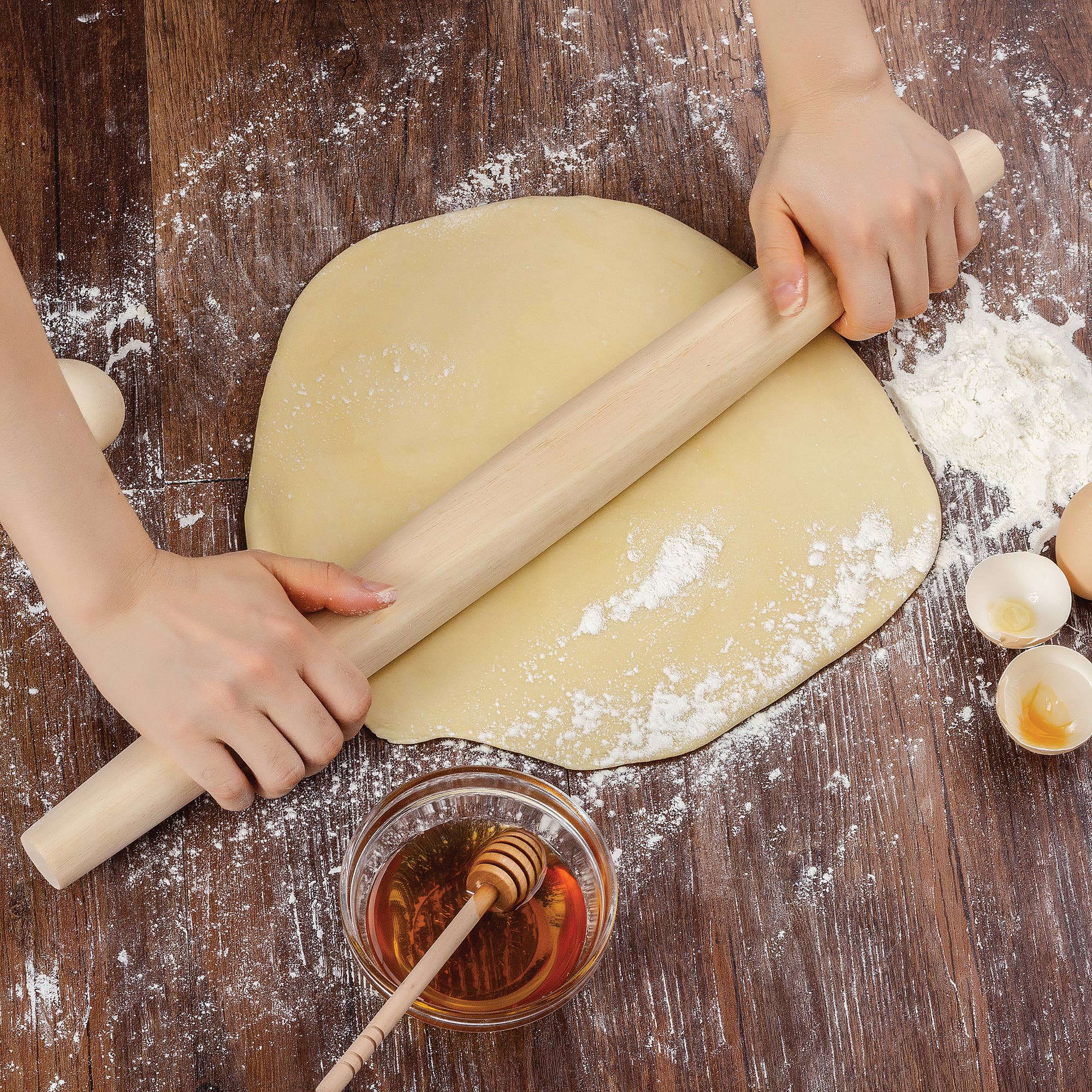 Person rolling out dough on a wooden surface with flour and a bowl of honey.