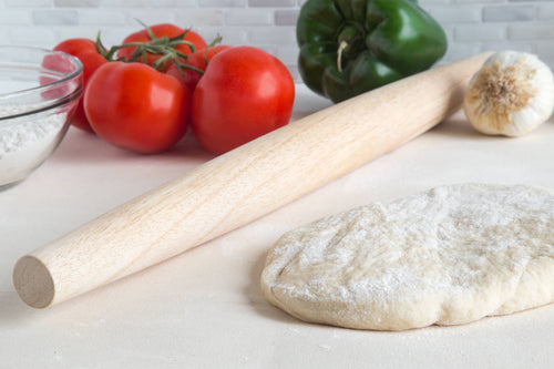 Pasta-making ingredients including tomatoes, bell pepper, garlic, and a rolling pin on a white surface.