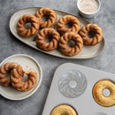French twist shaped donuts on a plate and platter with the baking pan nearby on a gray surface.