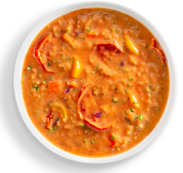 Tomato soup with vegetables in a white bowl on a white background
