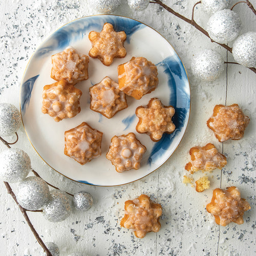 A plate of small cakes shaped like snowflakes on a white surface decorated with silver balls.