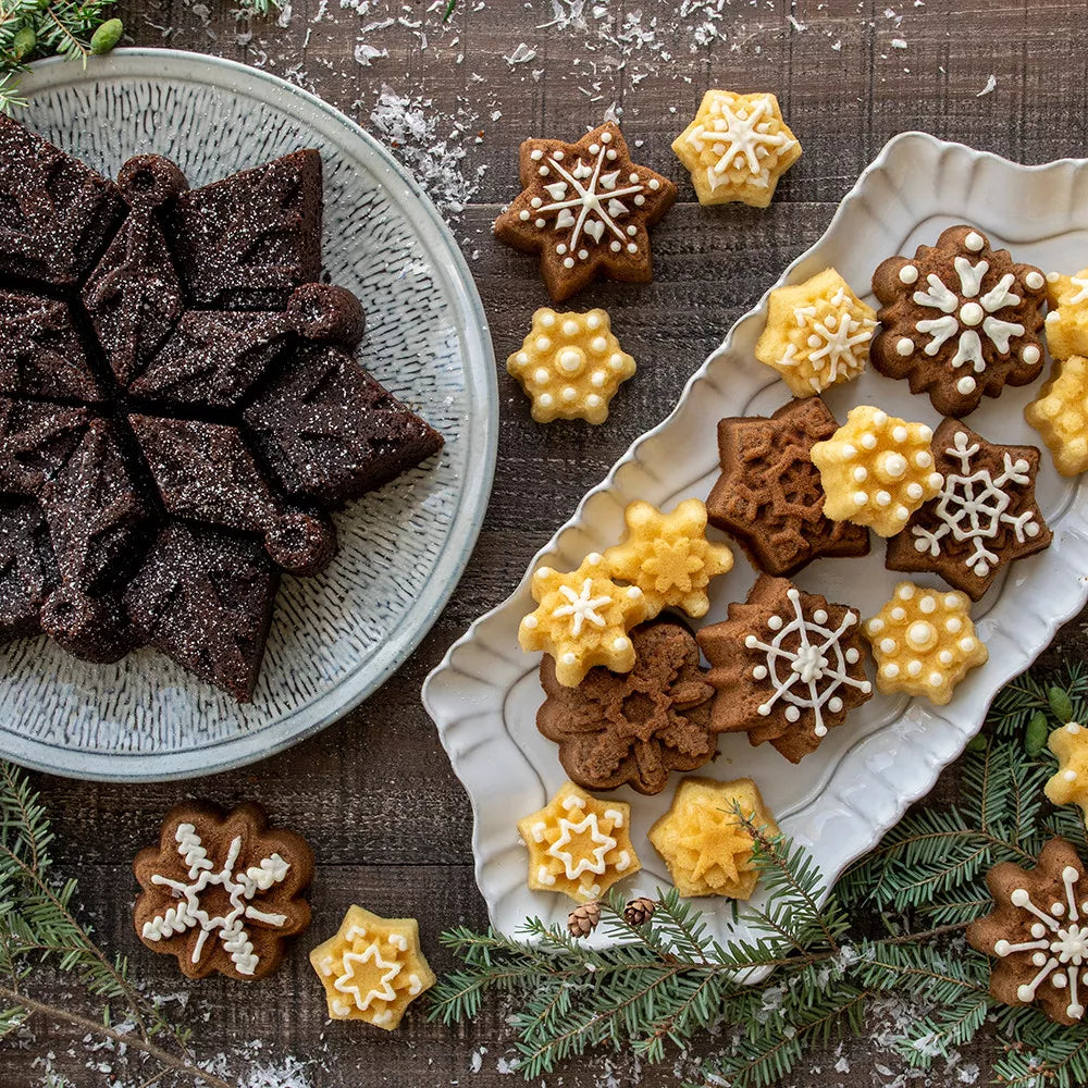 Decorative little cakes shaped like snowflakes on a wooden surface with greenery.