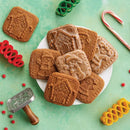 Decorative gingerbread cookies on a plate with a cookie stamp and candies on a green background