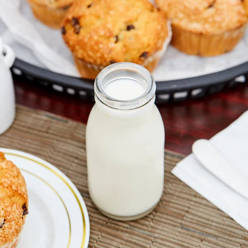 Glass bottle of milk on a table with muffins in the background