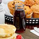Stack of pancakes with syrup and muffins in the background