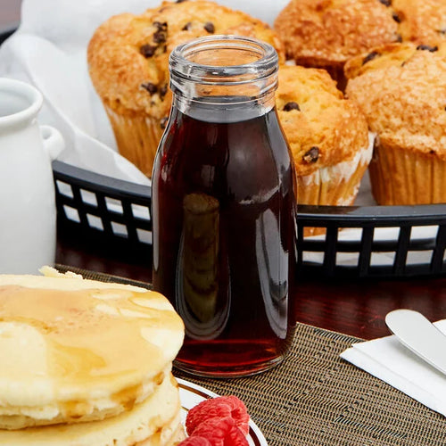 Stack of pancakes with syrup and muffins in the background