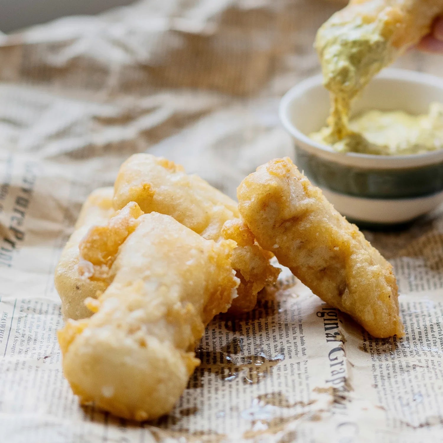 Fried food items being dipped into a green sauce on newspaper