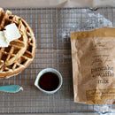 Waffle with butter, syrup, and a bag of Finch & Fennel pancake and waffle mix on a cooling rack.