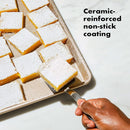 A person lifting up a lemon bar from a baking sheet and text noting the ceramic-reinforced non-stick coating.