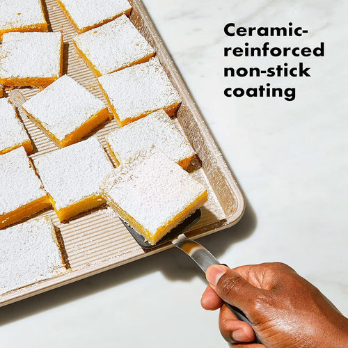 A person lifting up a lemon bar from a baking sheet and text noting the ceramic-reinforced non-stick coating.