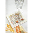 A napkin with autumn artwork and the word 'grateful' next to a paper placemat and a drinking glass on a white surface.