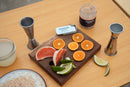 A jar of sea salt with sliced fruit and bar accessories on wooden surfaces.