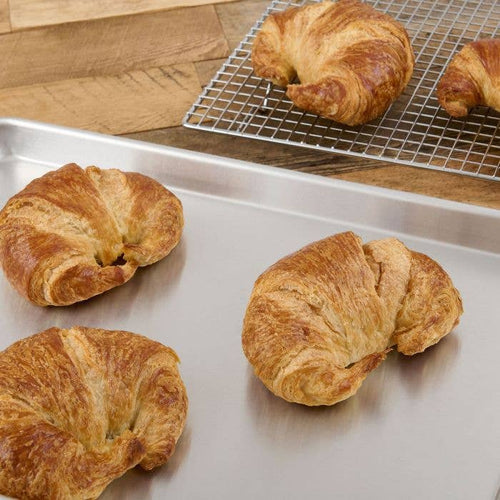 Croissants on a metal tray with one on a cooling rack.