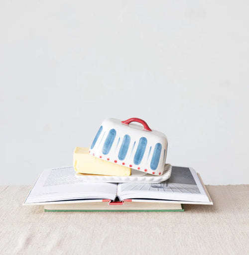 A hand painted butter dish with butter inside on top of books on a neutral background.